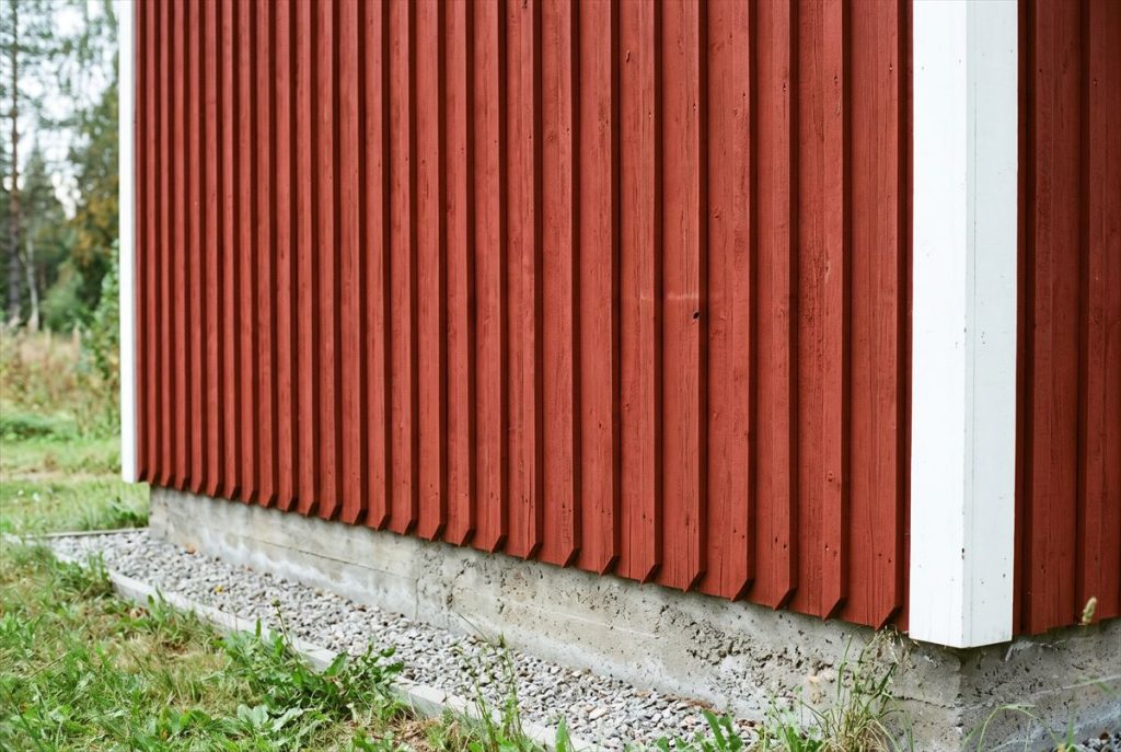 Punaiseksi maalattu lomalaudoitus, jonka alareuna päättyy betonisokkelin yläpuolelle